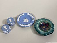 All four pottery pieces arranged side by side: Moorcroft ashtray with floral design, two Wedgwood pill boxes, and a Wedgwood ashtray
