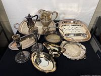 Entire set of vintage silver plated servingware including trays, candleholders, pitcher, gravy boat, and bowls arranged on table.