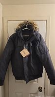 Full frontal view of the charcoal winter jacket with hoody, hanging on a hanger showing brand tag attached.