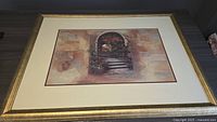 Framed picture showing an image of stone stairs with flowers under an archway, gold textured frame and cream matting.