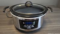 Full view of the Hamilton Beach digital slow cooker showing stainless steel body, black handles on each side, and glass lid with black handle.