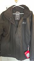 Front view of the black Helly Hansen jacket hanging on hanger showing zipper and HH logo
