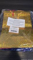 Gold holographic gift bag with red ribbon handles packed in plastic.