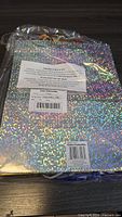 Holographic gift bags stacked and wrapped in plastic showing square reflective patterns and a label on top