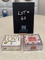 Photo showing two CD compilation box sets titled 'Classic Love' and 'Best of Original Oldies' with a black sign reading LOT# 63 in background
