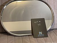 Oval chrome mirror shown resting, reflective surface visible, with no damage apparent.