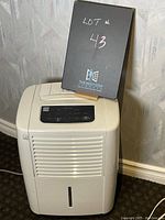 Front and slightly side angled view of the Kenmore dehumidifier with lot number sign placed on top.