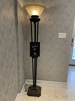 Full view of the dark brass floor lamp showing three-legged stem, decorative base, and frosted glass lamp shade.
