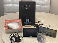 Lot containing Garmin nüvi 66 LMT GPS navigator, Acu-Rite weather system with LED display, cables, and accessories on a table with a black lot identifier board