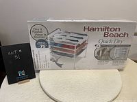 Hamilton Beach Quick Dry 4-Shelf Garment Drying Station boxed in original packaging showing product image and branding.