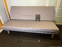 Front view of IKEA Beddinge Lovas futon sofa bed in used condition with grey quilted fabric cover and metal legs.