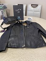 Black leather Esprit Sport women's jacket and black leather fanny pack displayed on table with white chairs in background.