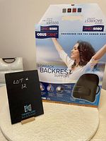 Photo of black Obusforme low backrest support box with product branding and usage image, placed upright with a small chalkboard showing lot number.