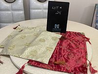 Four decorative pillow cases displayed on a table, three cream with gold patterns and one vibrant red with gold patterns and tassels