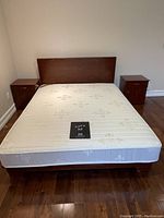 Full view of the queen size bed frame with mattress and headboard, flanked by two wooden nightstands.