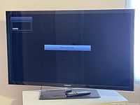 Samsung TV on rectangular stand with remote control on the base. Screen on showing 'Check signal cable' message.
