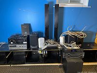 Full view of speakers, electronics and cables on black shelf against blue wall