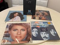 Four vinyl LP records displayed on round table showing cover art for Olivia Newton-John, Donna Summer, Mood Indigo, and Tony Orlando & Dawn albums.