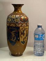 Front angle of antique cloisonné hand painted vase with water bottle for scale.