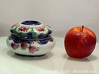 Side view of Nippon porcelain hair receiver with floral hand painted design next to an apple for size reference.