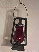 Front view of antique railroad lantern with visible ruby glass chimney and metal frame, hanging by its handle.