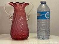 Full view of cranberry optic glass vase next to water bottle for scale, showing size and color.