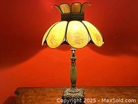 Full view of the floral slag glass table lamp against a red background with wooden surface.