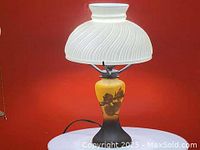 Table lamp with milk glass shade illuminated, showing floral design on the base.