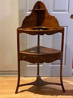 Front view of the Georgian style mahogany corner wash stand showing triangular shape with wash basin hole, two smaller recesses, drawer and lower shelf.