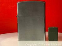 Closed giant Zippo lighter and smaller standard Zippo lighter side by side for size comparison.