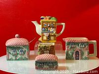 Four pottery items displayed together against a red background: a teapot, cream jug, sugar bowl, and pepper shaker, all decorated with cottage kitchen themes.