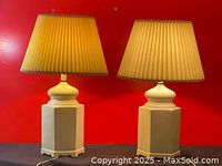 Pair of porcelain milk vase table lamps with beige pleated shades on a black surface against red background