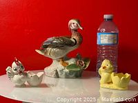Wide shot featuring the large duck figurine and two small bird-shaped ceramic egg cups with a water bottle for scale