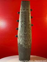 Porcelain oriental vase front side showing hand painted Chinese characters and design, with four small round handles on the neck, set against a red background.