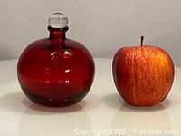 Ruby red glass blown bottle about 4 inches high shown beside an apple for scale.