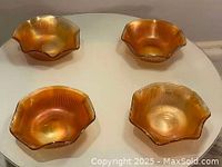 Four amber iridescent carnival glass bowls with ruffled edges, placed on a white round table.