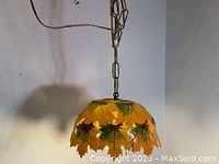 View of vintage ceramic hanging lamp with warm yellow light illuminating hand painted maple leaf design.