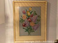 Frontal image of the vintage cross stitch floral bouquet artwork framed in light wood with glass, measuring 21 by 26 inches.