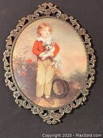 Front view of ornate brass oval frame featuring a painting/print of a Victorian child holding a small dog.
