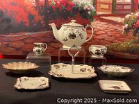 Complete view of the tea set displayed on a table against a backdrop, showing teapot, serving trays, cream pitcher, sugar bowl, and plates with silver leaf pattern