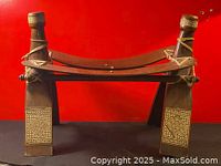 Front view of a vintage Egyptian wooden camel stool showing carved geometric panels on front legs and curved top seat with rope bindings.