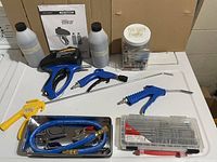 Full overview of the lot showing the abrasive spot blaster gun, sandblast sand jugs, multiple air guns and accessories, screwdriver bit set, and jar of air gun parts.