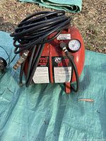 Photo of red portable air tank with black hose coiled on top, pressure gauge visible on front.