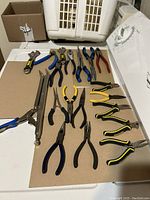 Top view of assorted pliers arranged on cardboard surface showing variety and handle colors.