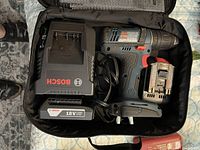 Open Bosch carrying case with cordless drill, battery, charger, and cables inside