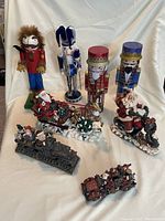 Four nutcracker figures in varied styles and two Santa Claus sleigh figurines in front, along with two miniature Christmas trains at bottom of scene