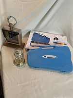 Overview of two clocks - one silver and wood with Roman numeral face, one dome pendulum clock, blue glockenspiel case and box.