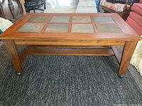 Front view of rectangular wood coffee table with slate tile inlay and casters on carpet.
