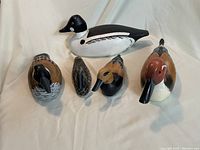 Front view of five assorted hand carved wooden duck figurines, showing varied species and color patterns.
