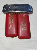 Photo showing two Hohner Golden Melody harmonica cases side by side with chrome covers and red plastic bodies, lying on white surface.